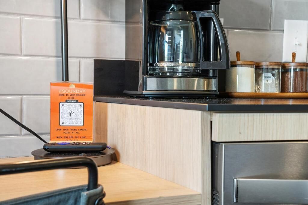 A kitchen area with a coffee maker, a QR code sign, and jars on the counter.
