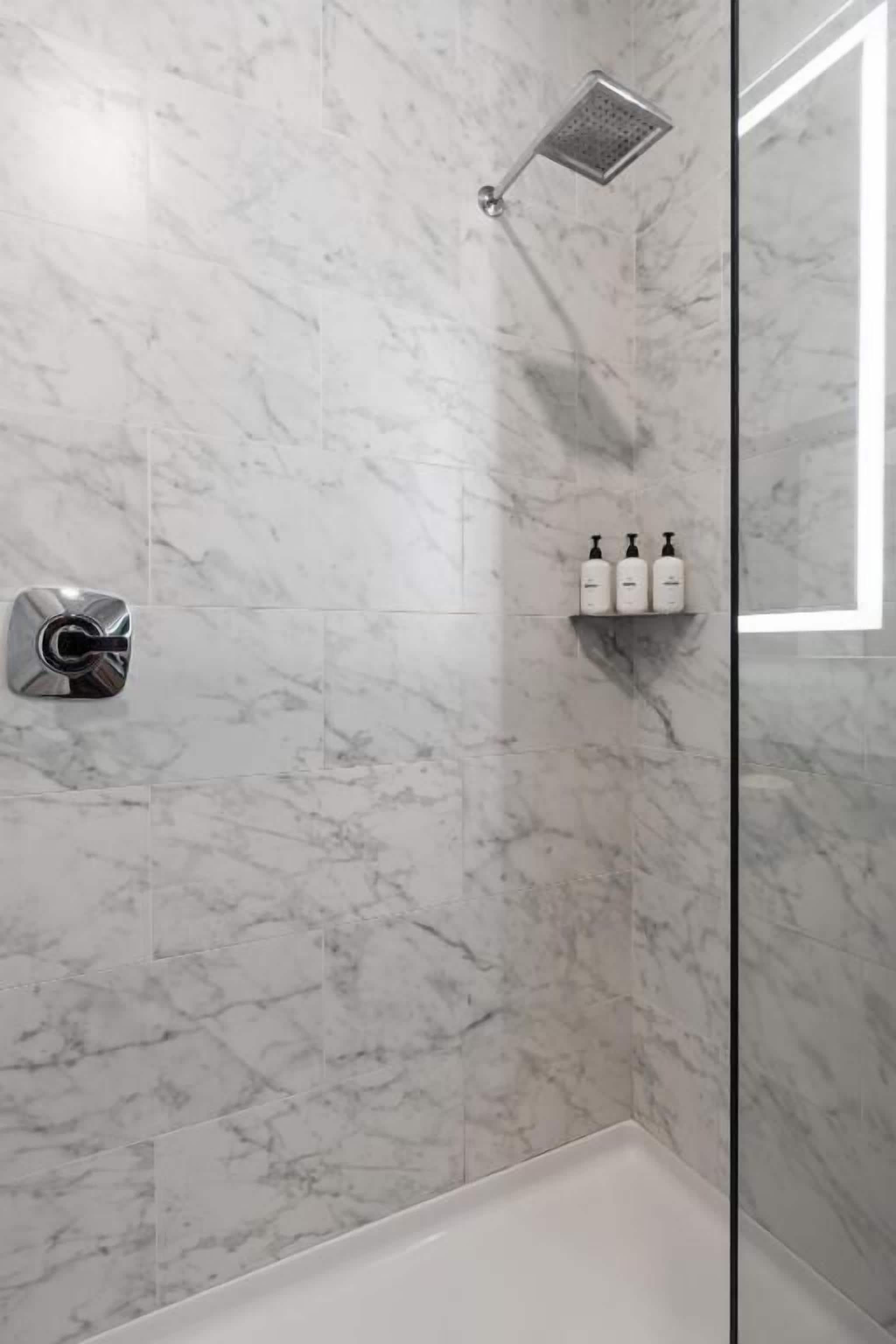 A modern bathroom with marble tiles, a showerhead, and a soap dispenser shelf.