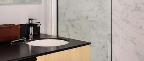 A bathroom with a marble backsplash, a sink with a black countertop, and a mirror with a light frame.