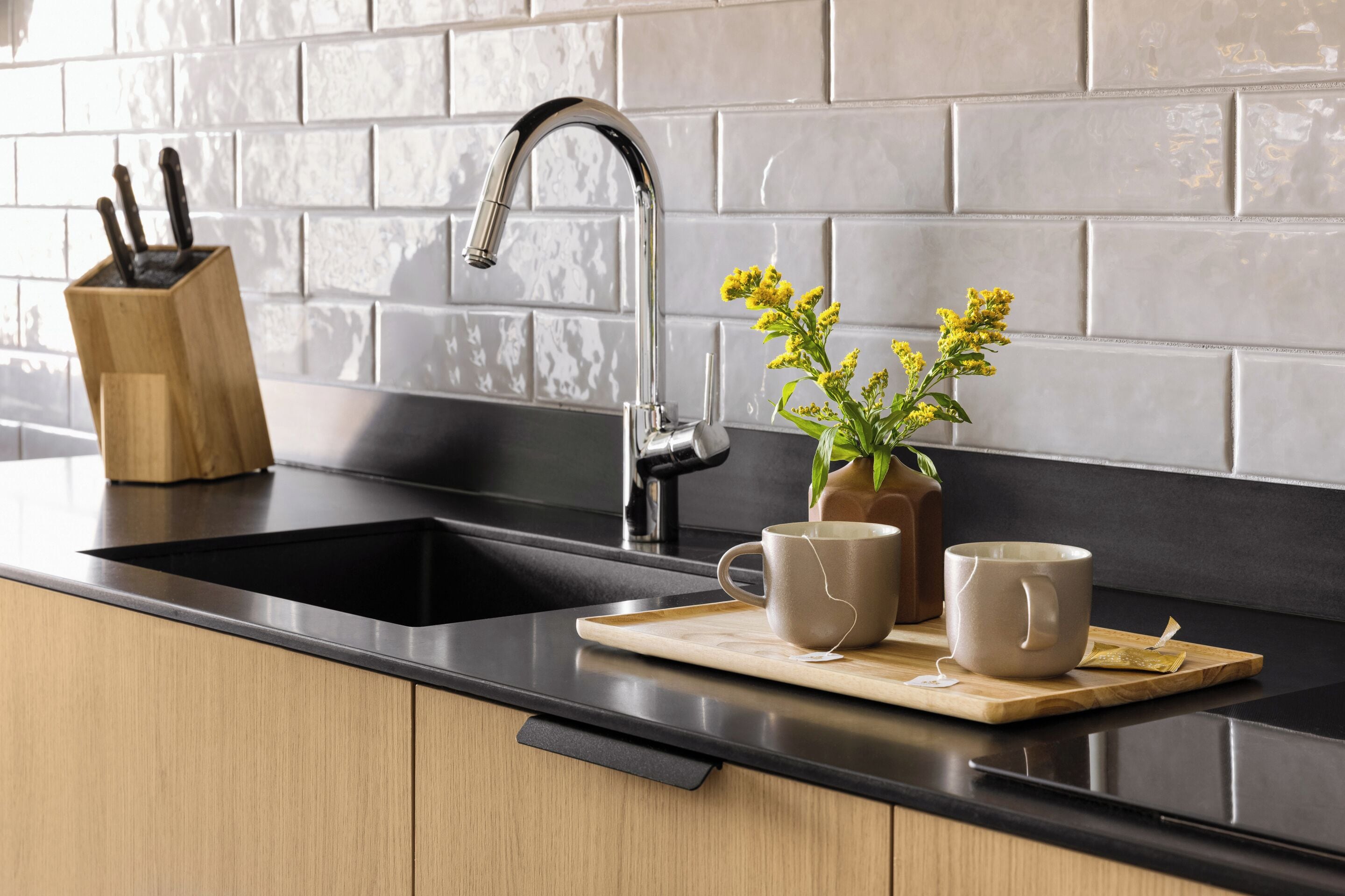 Een moderne keuken met een zwart aanrecht, een roestvrijstalen spoelbak en een houten messenblok.