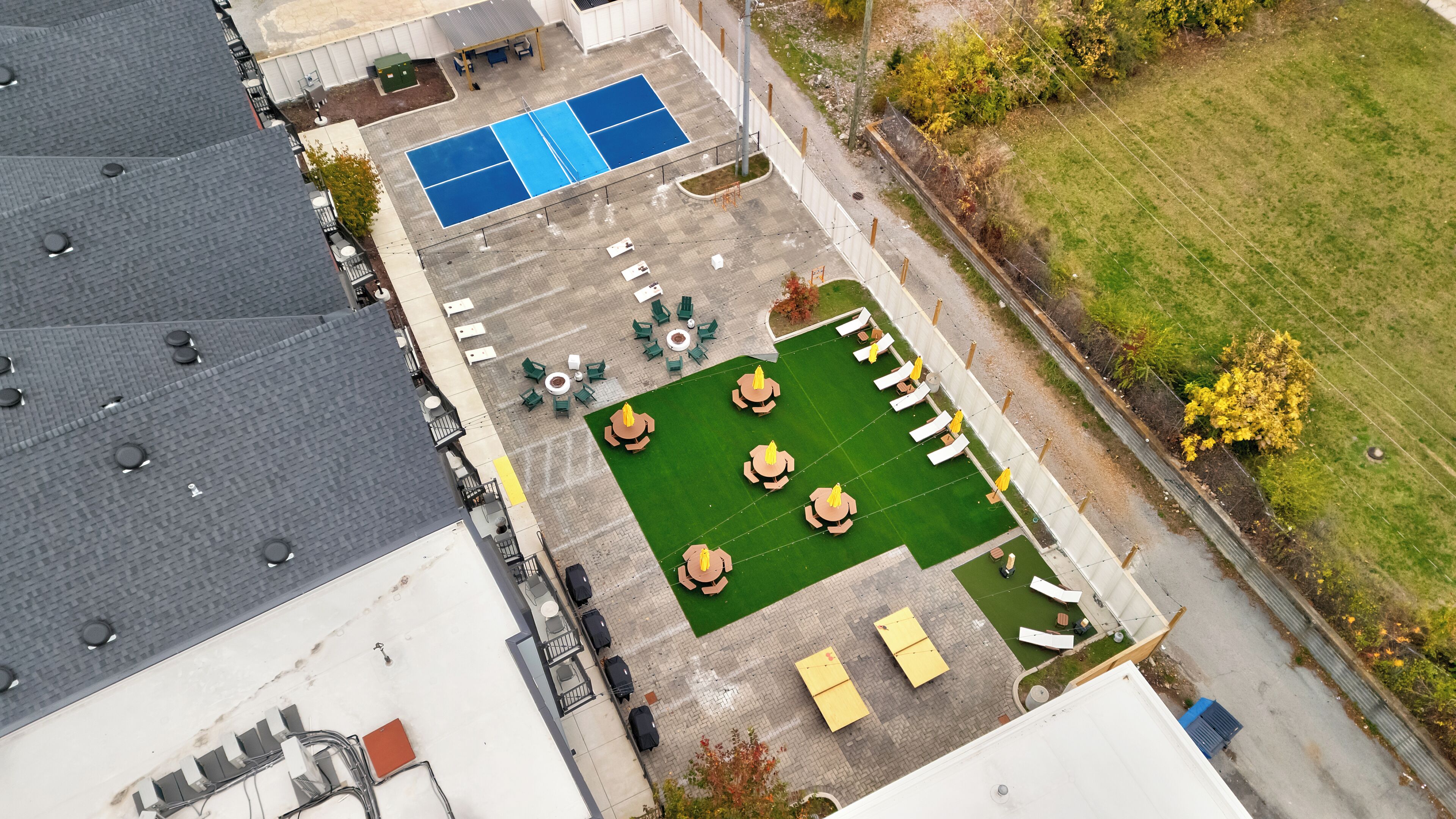 An aerial view of a hotel with a rooftop pool, outdoor seating area, and a tennis court.