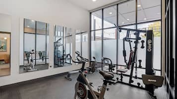 Un gimnasio con equipo de ejercicio, ventanas amplias y un muro espejado.