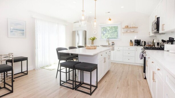 A modern kitchen with white cabinets, a central island, and bar stools. - Modern Renovated Retreat w/ Pool in North Cape May (Lower Township)