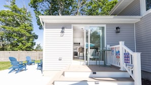A covered outdoor area with a deck, outdoor seating, and a glass door leading to a kitchen. - Modern Renovated Retreat w/ Pool in North Cape May (Lower Township)