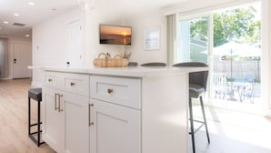 A modern kitchen with white cabinetry, a central island, and a large window overlooking a backyard. - Modern Renovated Retreat w/ Pool in North Cape May (Lower Township)