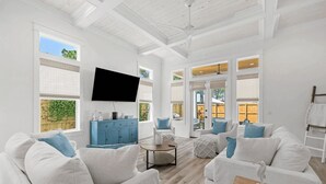 A spacious living room with white furniture, a blue cabinet, and a flat-screen TV mounted on the wall. - Sleeps 34! 2 Homes, Private Pools, Firepit, Golf Cart, Walk to Beach Seagrove San Juan by Avantstay (Santa Rosa Beach)