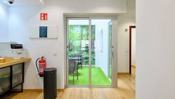 Habitación de hotel con puerta de vidrio corredera que da a un jardín, extintor, cesto de basura y escritorio con impresora.