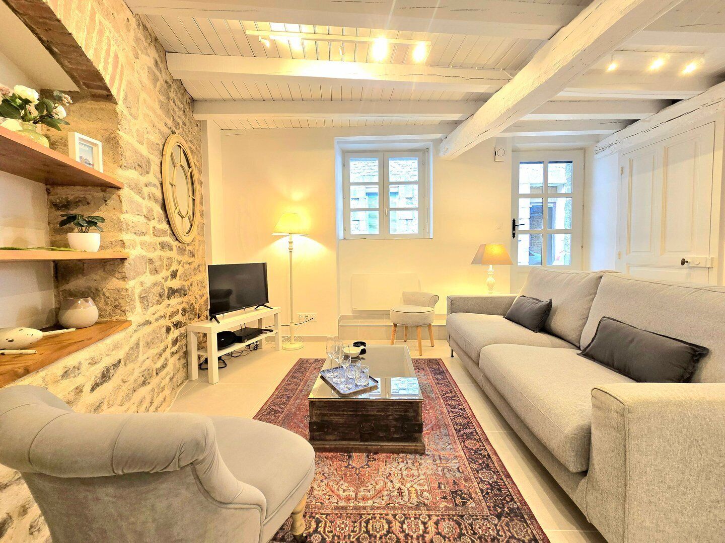 Una sala de estar con pared de piedra, televisor, sofá, mesa de centro y alfombra estampada.