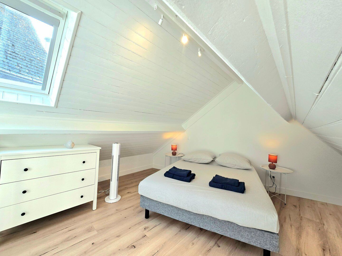 Una camera da letto con soffitto a volta, un letto con cuscini, un comodino con una lampada, una cassettiera e una finestra con vista.