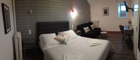 A hotel room with a large bed, a desk, a chair, and a radiator.