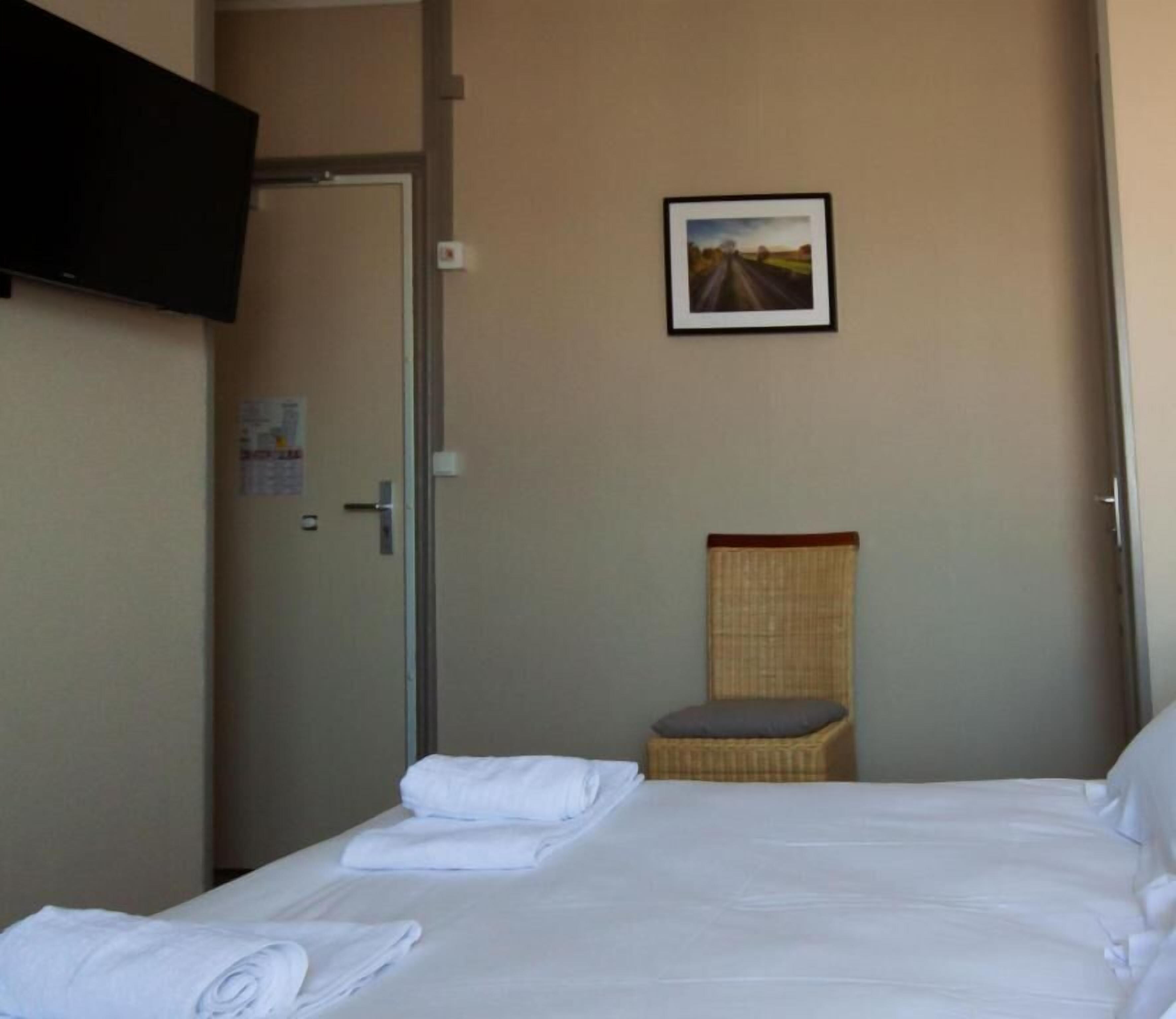 Een hotelkamer met een bed, een stoel, een televisie en een schilderij aan de muur.