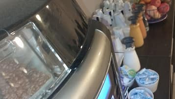 A coffee machine with a digital display, a glass container with nuts, and a fruit bowl on a counter.