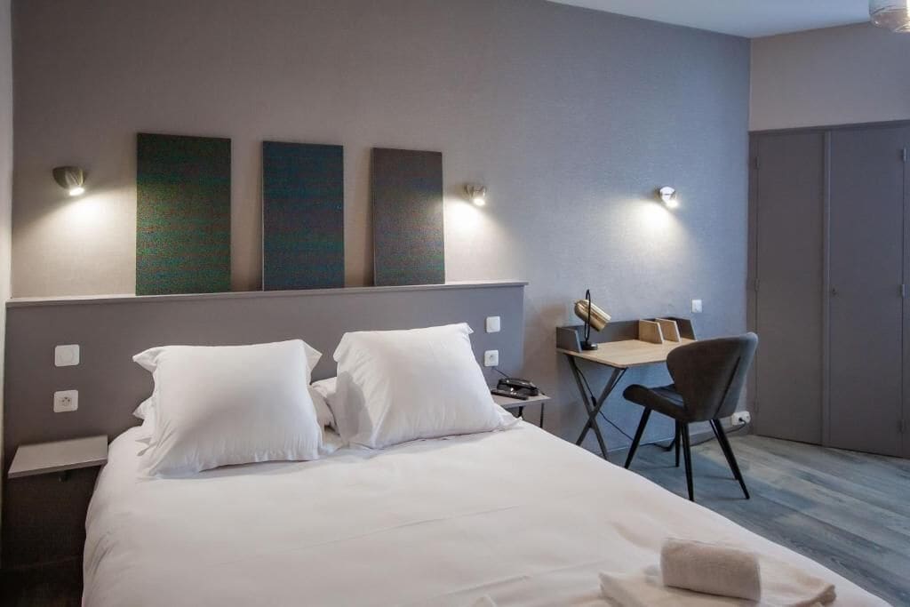 A modern hotel room with a large bed, a desk with a chair, and artwork on the wall.