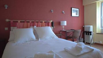 A hotel room with a large bed, a desk, a chair, and a radiator.