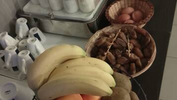 A kitchen counter with a fruit bowl containing bananas, apples, and kiwis, a basket of nuts, and a container with jars of condiments.