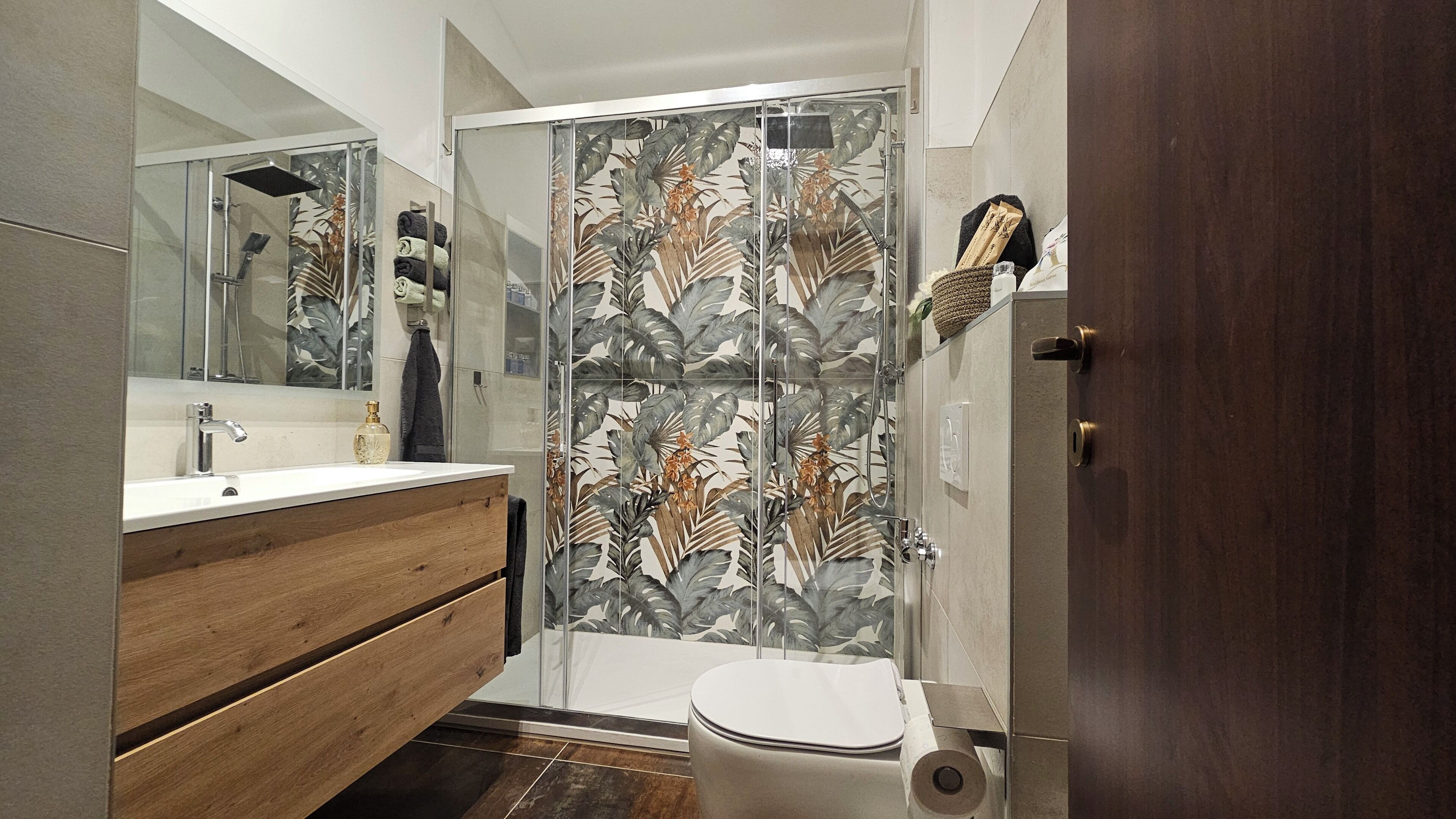 A bathroom with a wooden vanity, a glass shower enclosure with a leaf pattern, and a toilet.