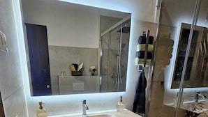 A modern bathroom with a large mirror, a white sink, wooden vanity drawers, and a glass shower enclosure. - Exclusive Family Vacation: High-Quality, Stylish Apartment in Milan, 10 Minutes from Gardaland (Venetien)