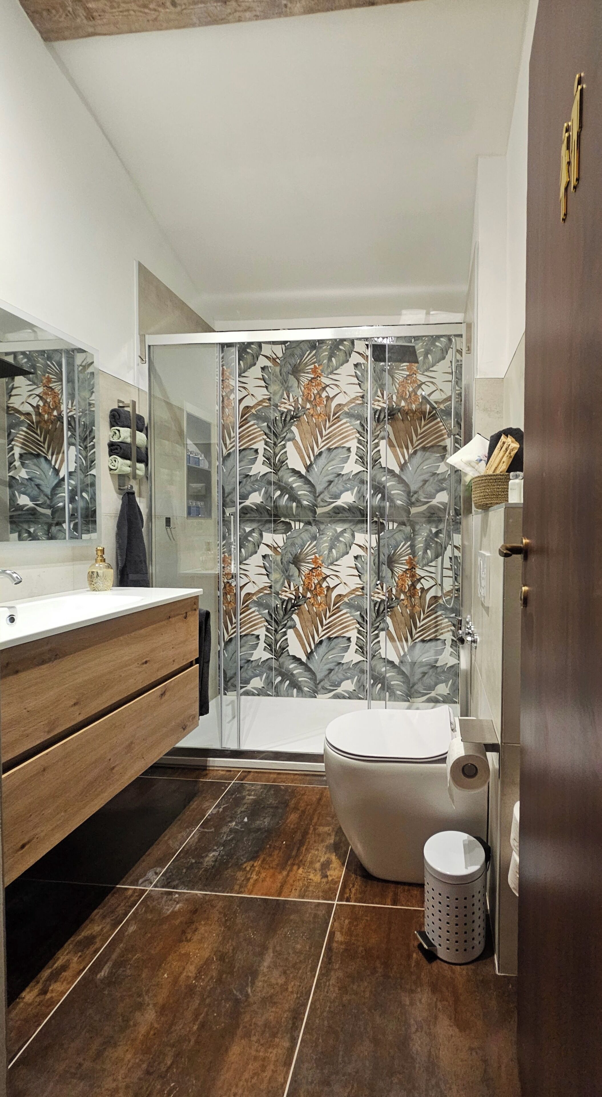 Ein Badezimmer mit einem Holzkosmetikschrank, einer Duschkabine mit Blattmuster und einer Toilette.