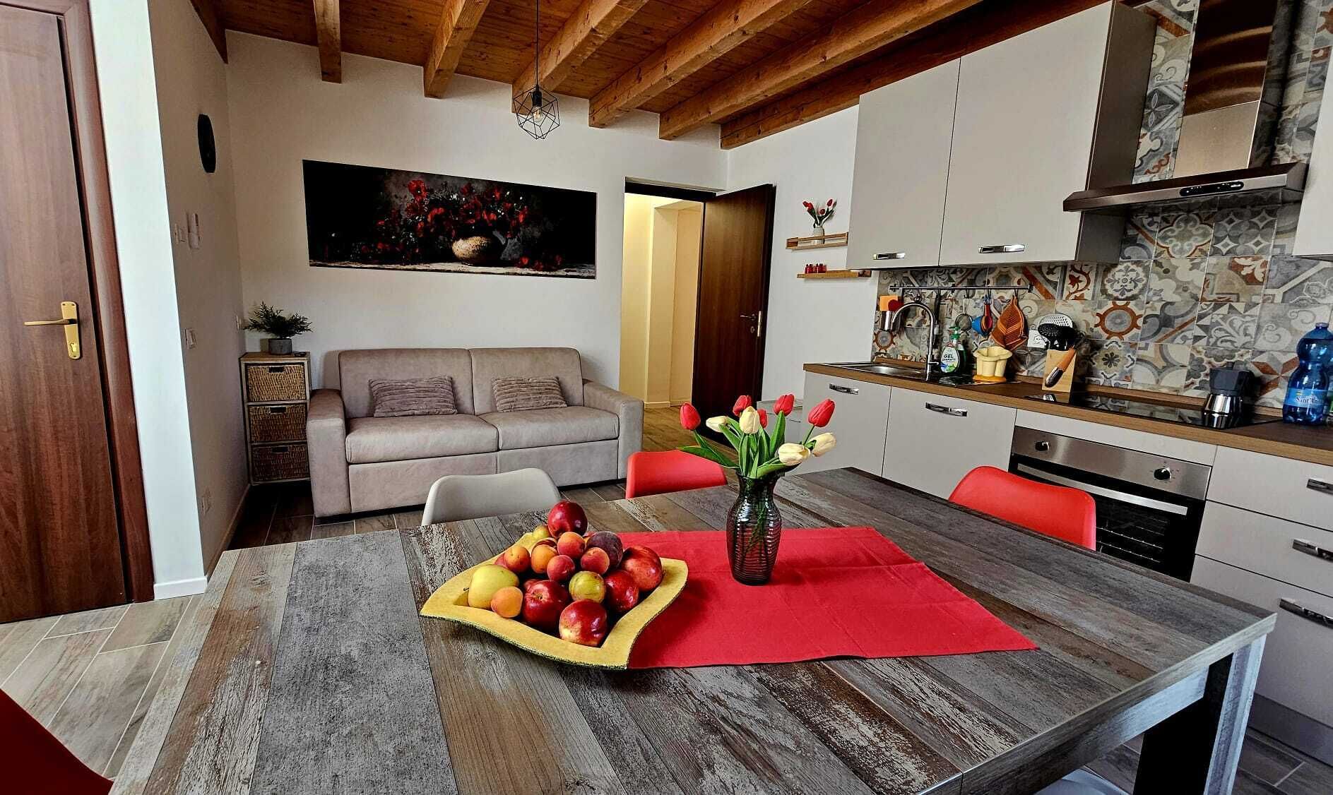Un comedor con una mesa de madera, un florero con flores y un frutero.