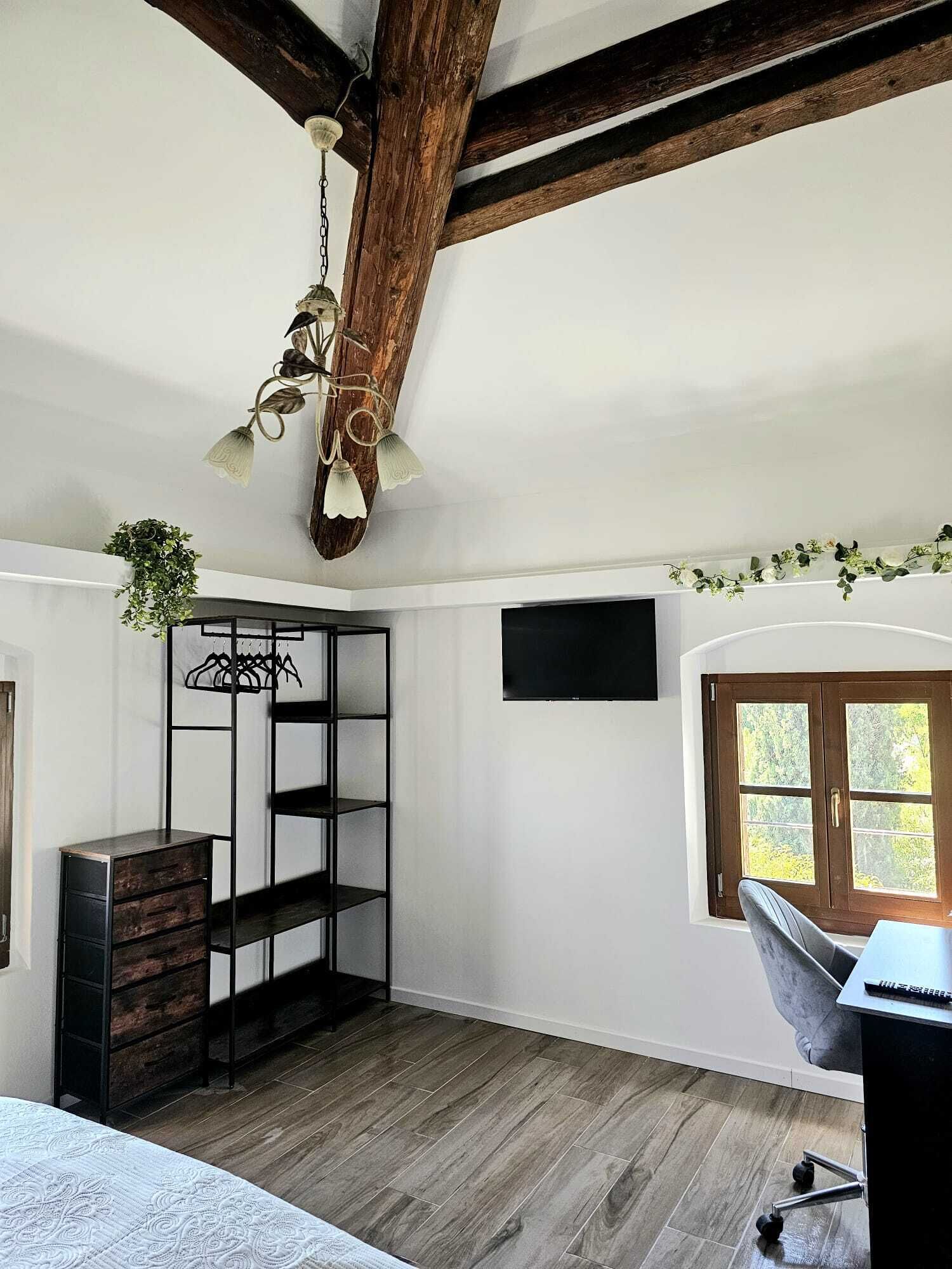 Une pièce avec un plafond en bois, un luminaire suspendu, une plante, un téléviseur fixé au mur et une fenêtre donnant sur un beau paysage.
