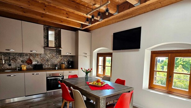 A modern kitchen with wooden beams, a dining area with red chairs, and a large window with a view of greenery. - Exclusive Family Vacation: High-Quality, Stylish Apartment in Milan, 10 Minutes from Gardaland (Venetien)