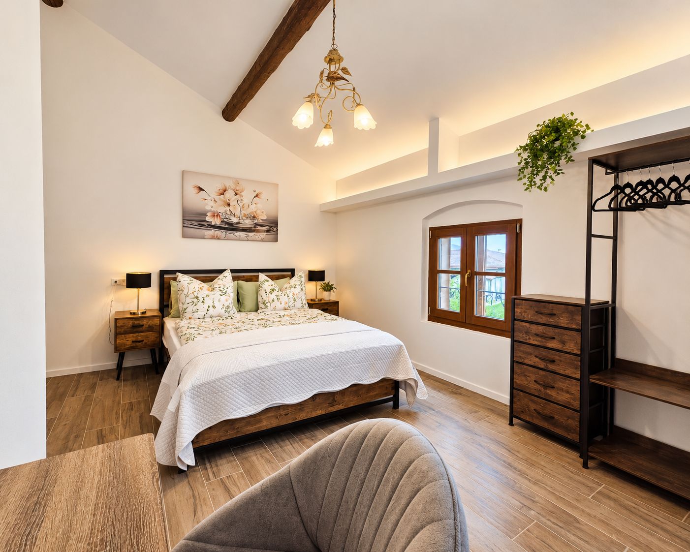 A bedroom with a bed, bedside tables, a hanging plant, a window, and a wooden ceiling beam.