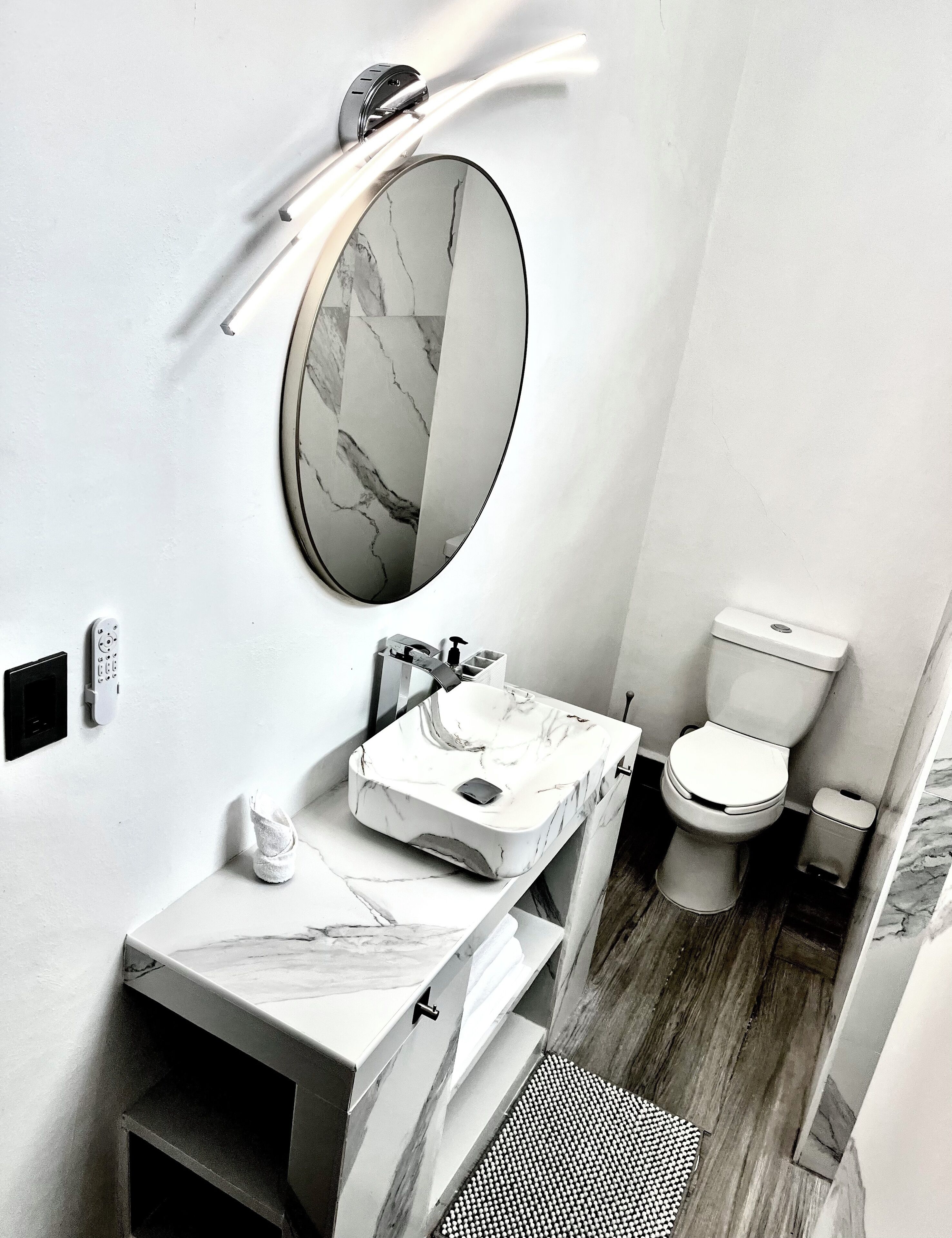 Un bany modern amb un lavabo de marbre, un mirall rodó, un vàter i una zona de dutxa.