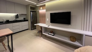 A modern kitchen with a built-in refrigerator, a flat-screen TV mounted on the wall, and a dining area with a table and chairs. - Apartamento Noroeste (Brasília)