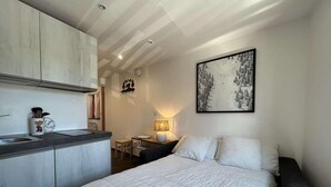 A compact room with a bed, a small desk, a chair, a lamp, and a painting on the wall. - 150m from ski slopes, 1st floor, view village, balcony, tv, ski locker, 20m², Montgenèvre (Montgenèvre)