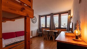 Une chambre avec un lit superposé, une table à manger avec des chaises, une horloge et une fenêtre avec des rideaux.
