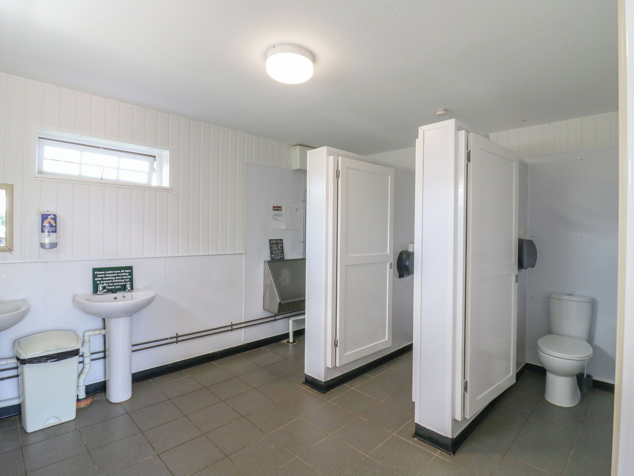 A bathroom with white walls, a window, a sink, a toilet, and a door.