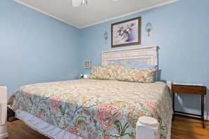 Une chambre à coucher avec une couvre-lit à motifs floraux, une tête de lit blanche, une table de chevet et une petite table de nuit.