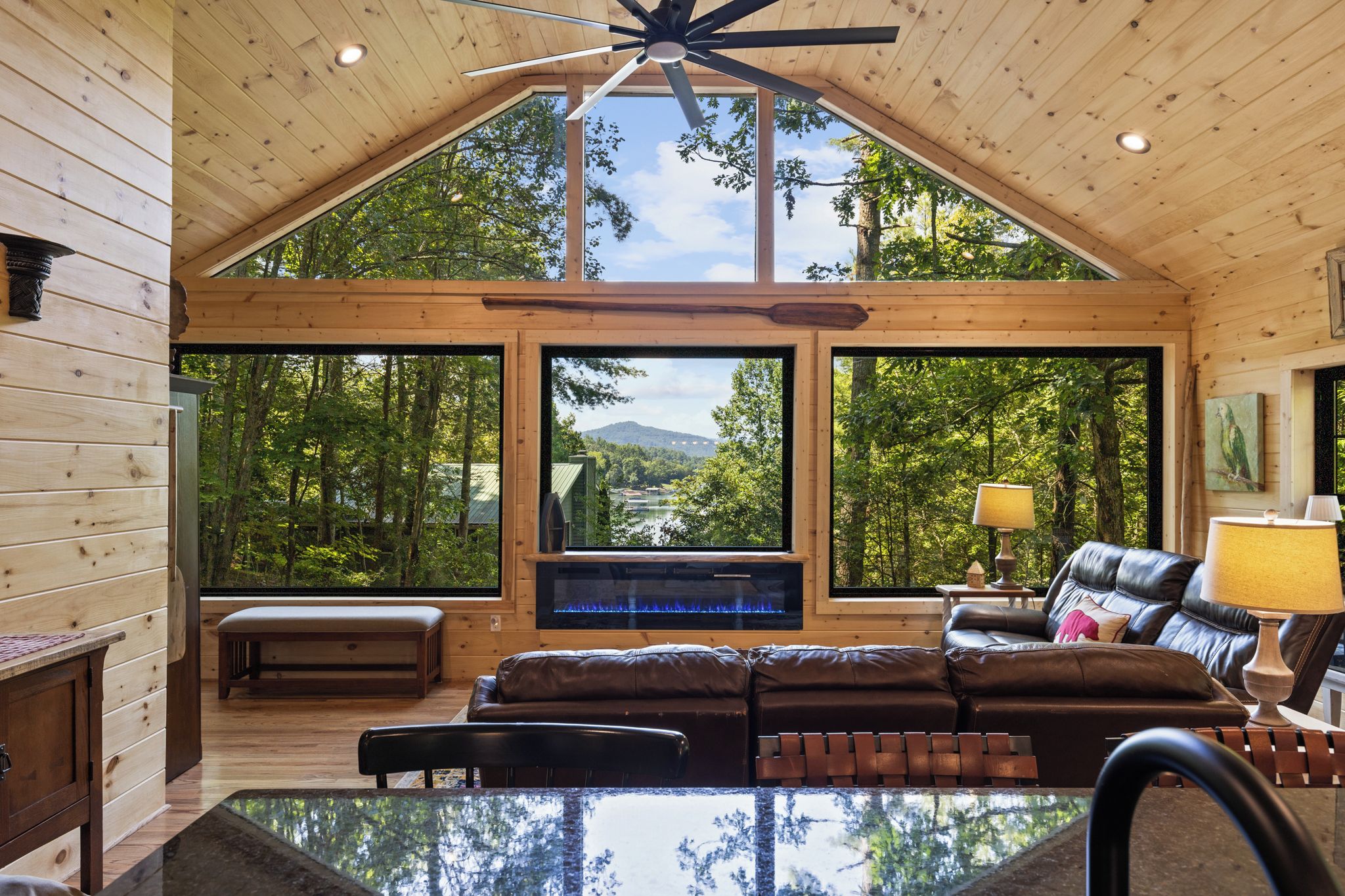 Ein geräumiges Wohnzimmer mit Kamin, Ledersofas und großen Fenstern mit Blick auf eine bewaldete Landschaft.