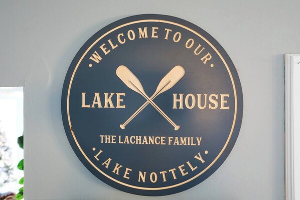 A circular sign with the text "Welcome to our Lake House The Lachance Family Lake Notteley."