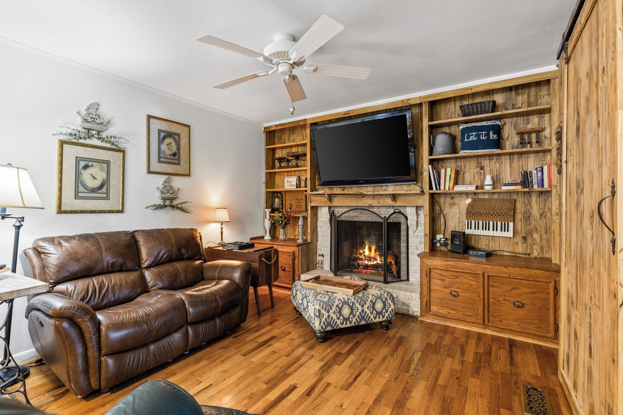 Una sala de estar con un sofá de cuero, chimenea, televisor y estanterías de madera con libros y objetos decorativos.