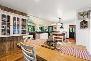Une table de salle à manger en bois avec des chaises, un coin cuisine avec une cuisinière et un buffet contenant de la vaisselle.
