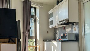 Een kleine keuken met een magnetron, een wastafeltje en keukenkastjes.