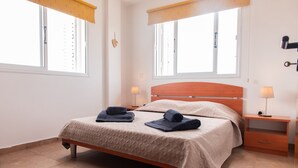 Ein ordentlich bezogenes Bett mit Holz-Kopfstück, zwei Nachttischlampen und einem kleinen Nachttisch mit Schublade.