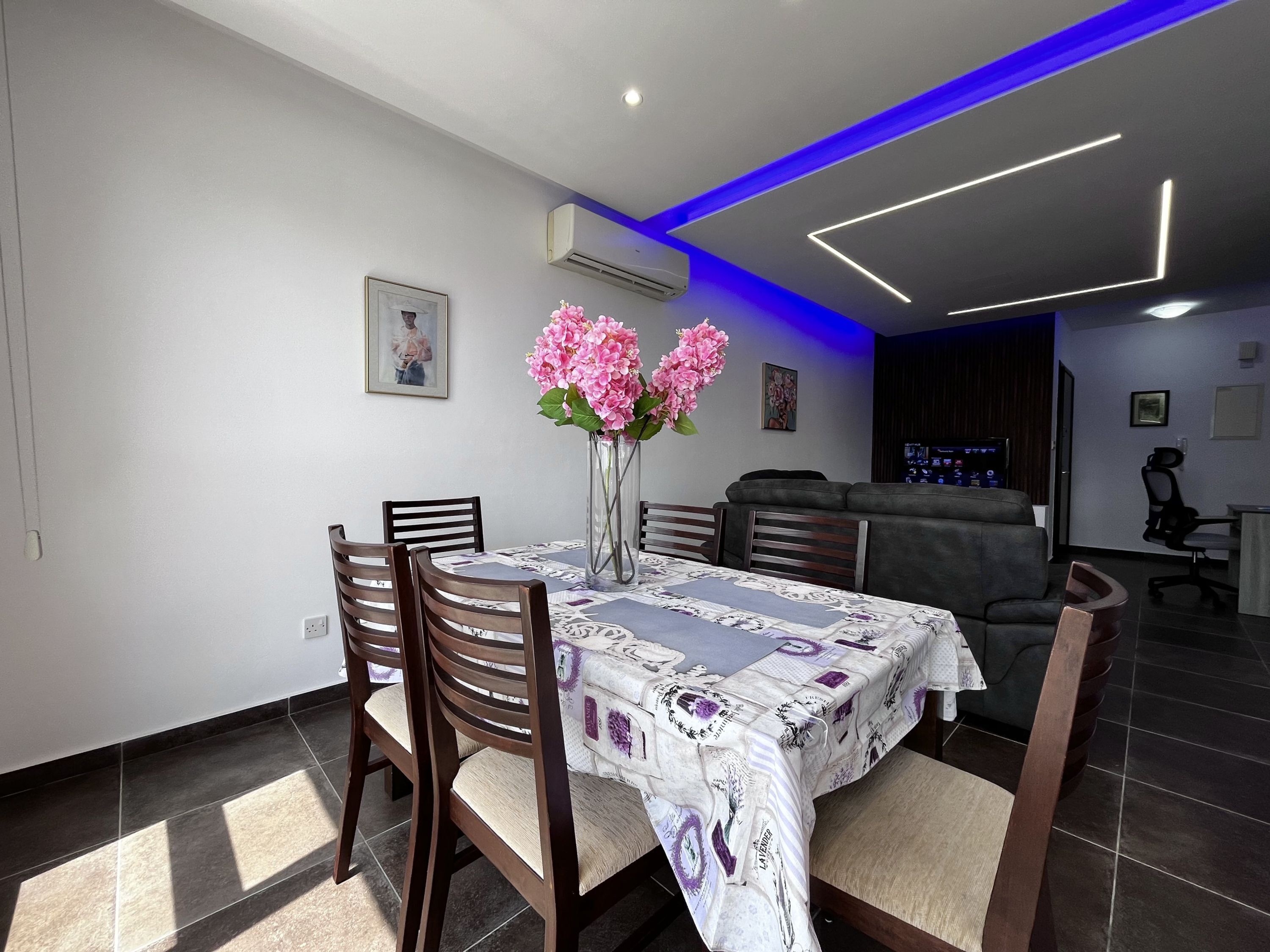 A dining area with a table set for four, surrounded by chairs, a vase with flowers, and a modern ceiling design.
