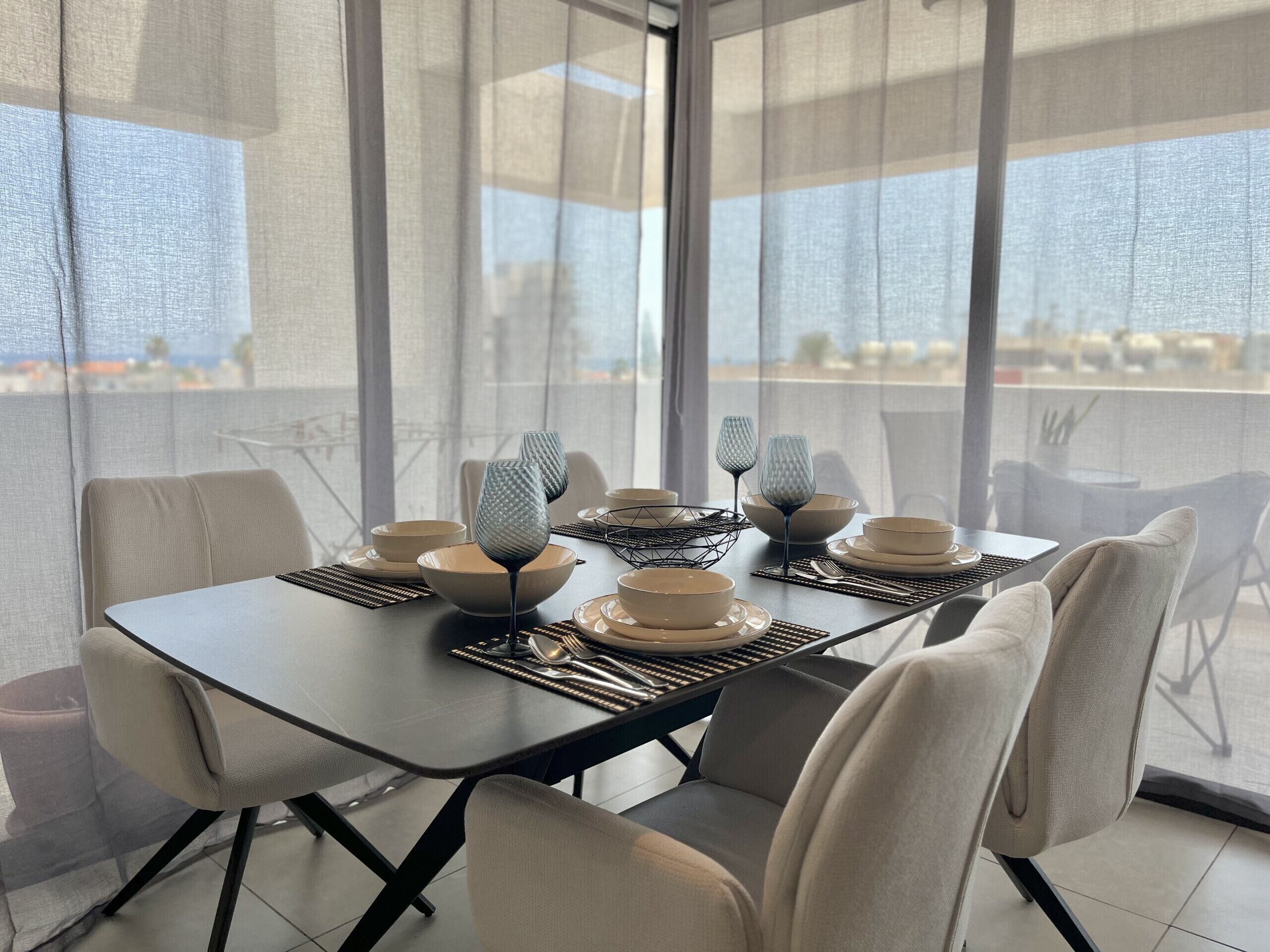 A modern dining area with a table set for four, featuring geometric glassware and neutral-toned plates and bowls.