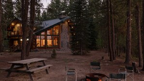 A log cabin with a stone exterior, large windows, and a fire pit in the yard. - Little Deschutes Wildlife Lodge - Nature's Cabin (La Pine)