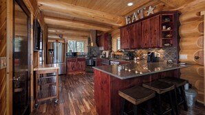 A spacious kitchen with wooden cabinets, a granite island, and a bar area. - Little Deschutes Wildlife Lodge - Nature's Cabin (La Pine)