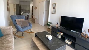 Una sala de estar moderna con un sofá, un sillón azul, una mesa de centro negra y un televisor sobre un mueble negro.