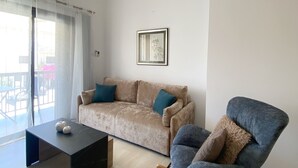 Una sala de estar moderna con un sofá color beige, un sillón mecedor azul, una mesa de centro negra y un ventilador de techo.