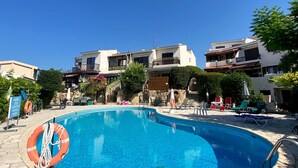 Piscina con sillas de descanso y un flotador salvavidas, rodeada de baldosas de piedra y edificios al fondo.