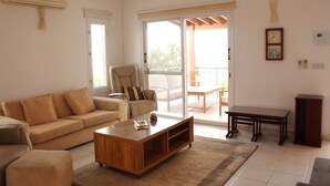 A living room with a sofa, coffee table, and a chair. There is a sliding glass door leading to an outdoor area. - 102 PAP - Stay Helios House (Mesa Chorio)
