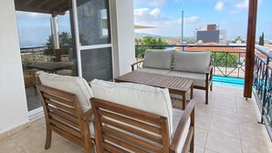 A covered patio with a wooden table and two chairs, a sliding glass door, and a view of the cityscape. - 102 PAP - Stay Helios House (Mesa Chorio)