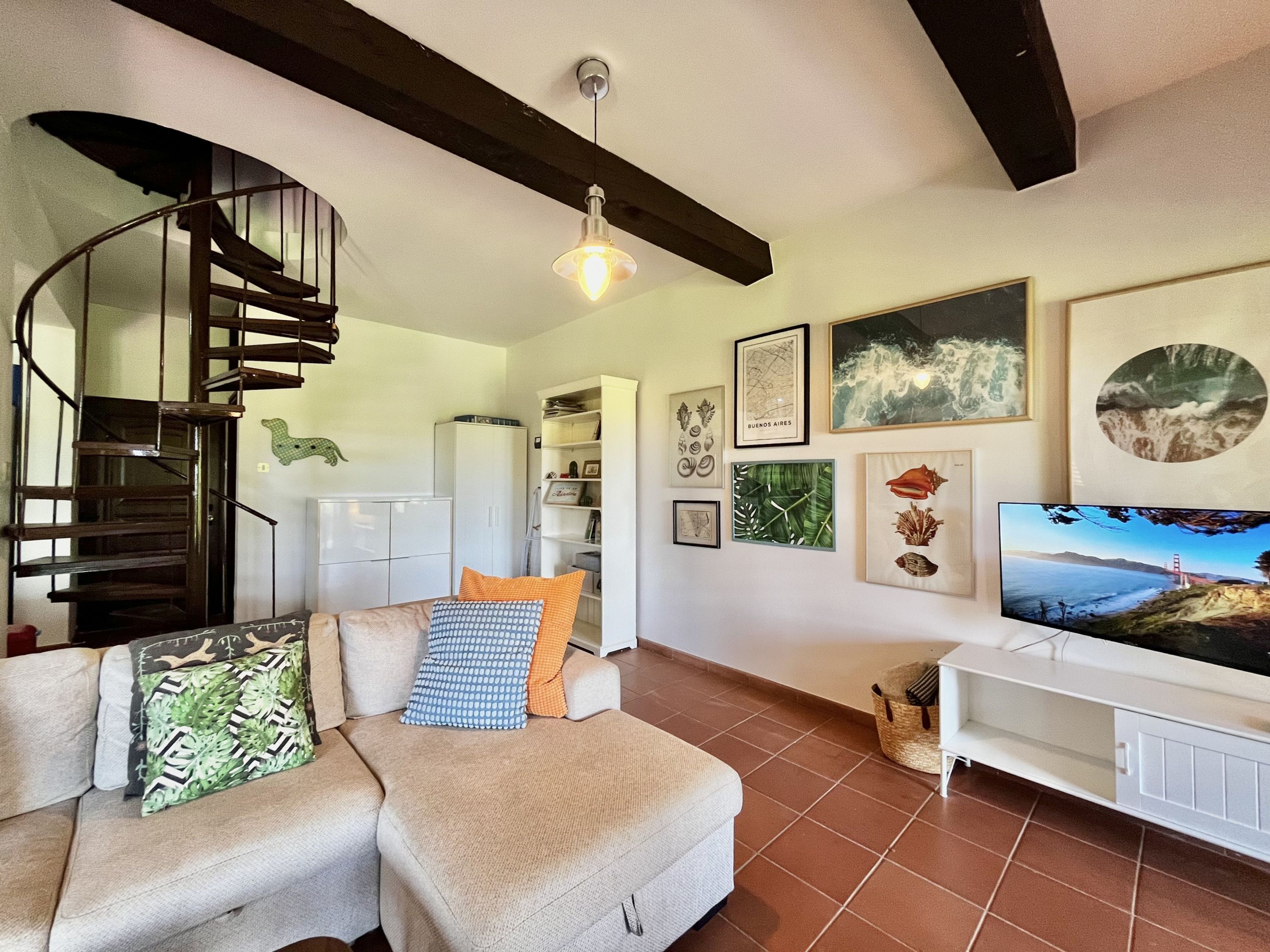 A living room with a sofa, a television, and a spiral staircase.