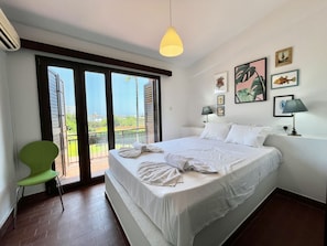 A bedroom with a bed, a green chair, a balcony with a view, and artwork on the wall. - 152 PER - Stay Perla House (Paralimni)