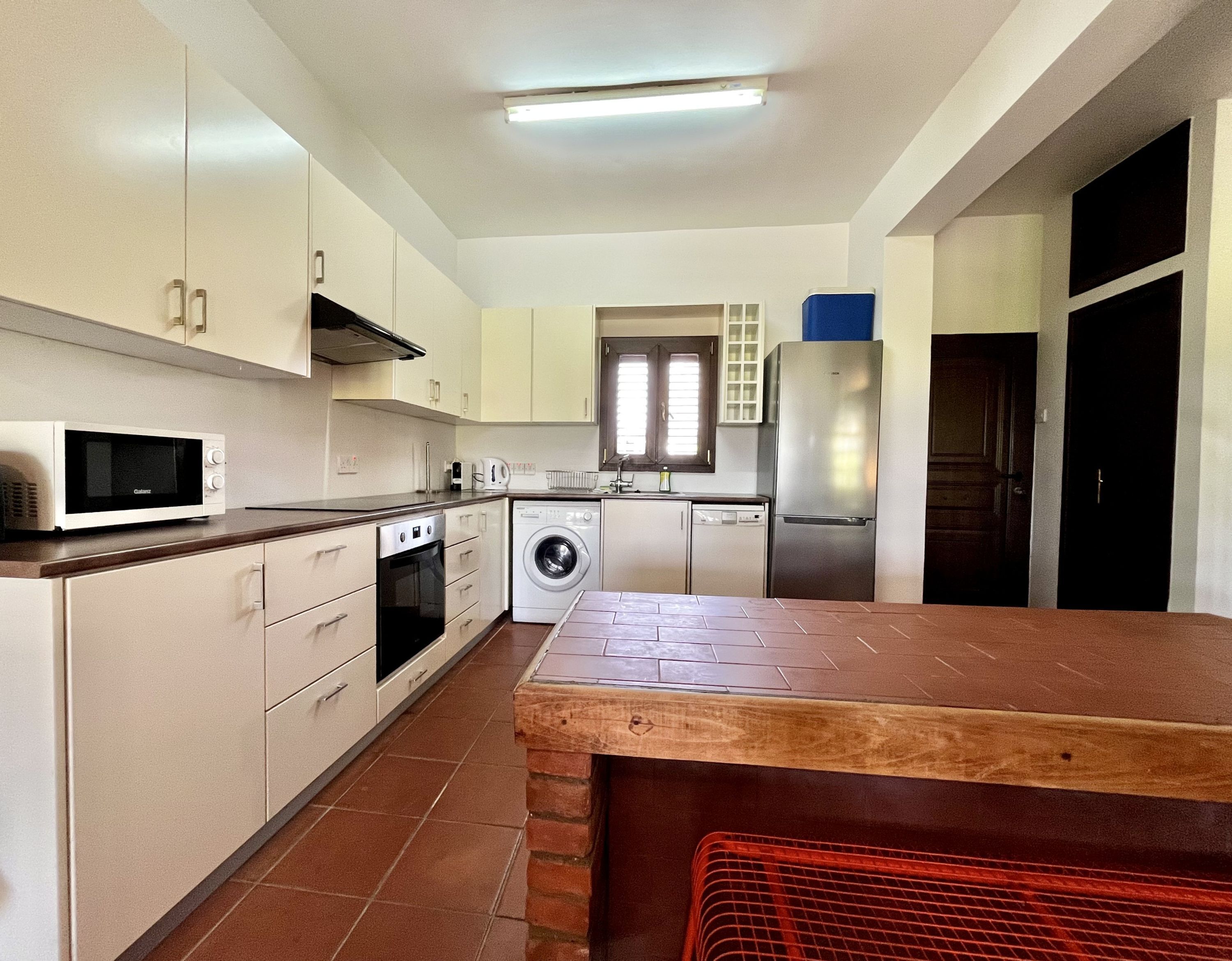 Una cocina con armarios blancos, microondas, lavadora, lavavajillas y refrigerador.